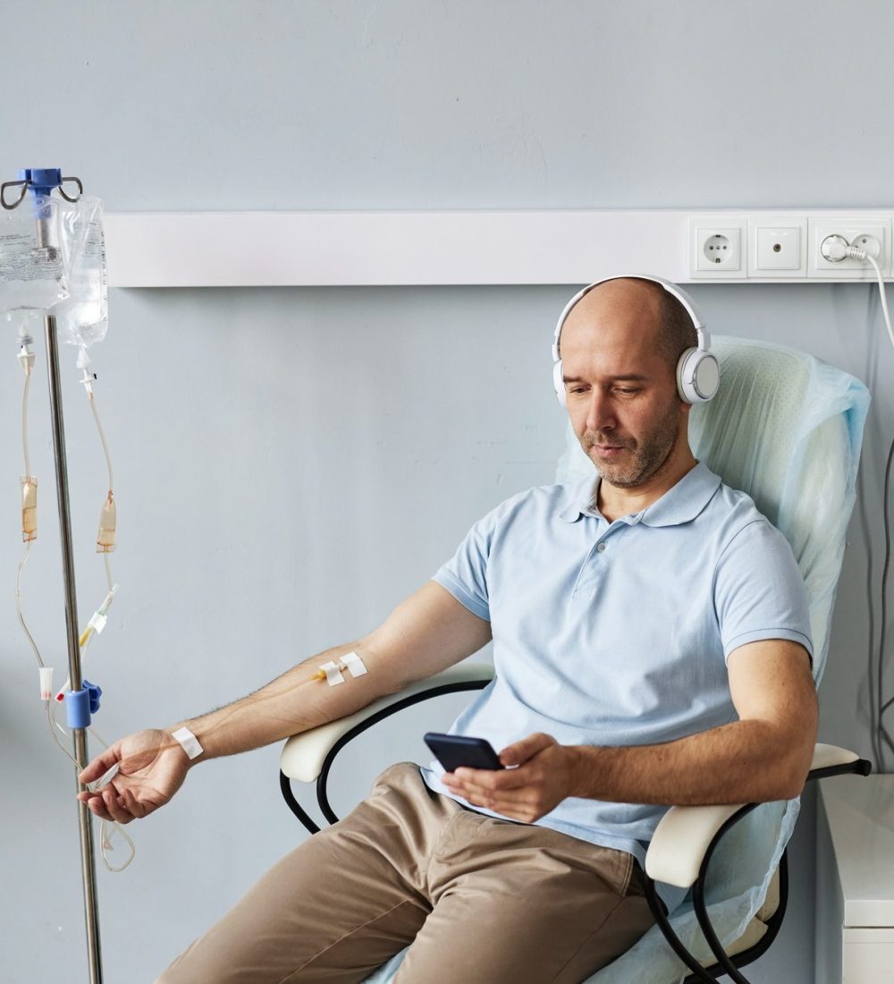 Minimal adult man with headphones during IV drip treatment in clinic Minimal adult man with headphones during IV drip treatment in clinic